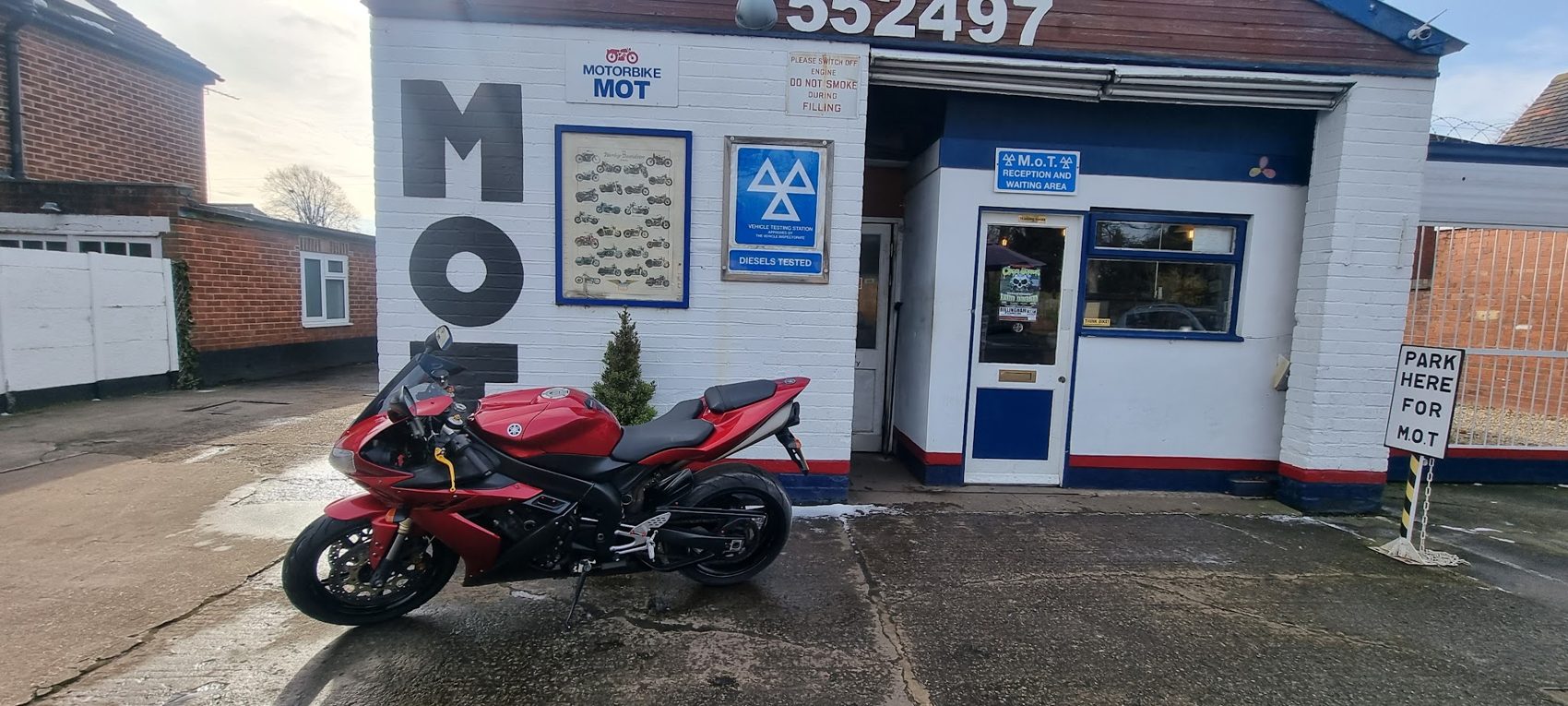 The white painted front of Bank Top Garage with a red motorbike parked outside the door