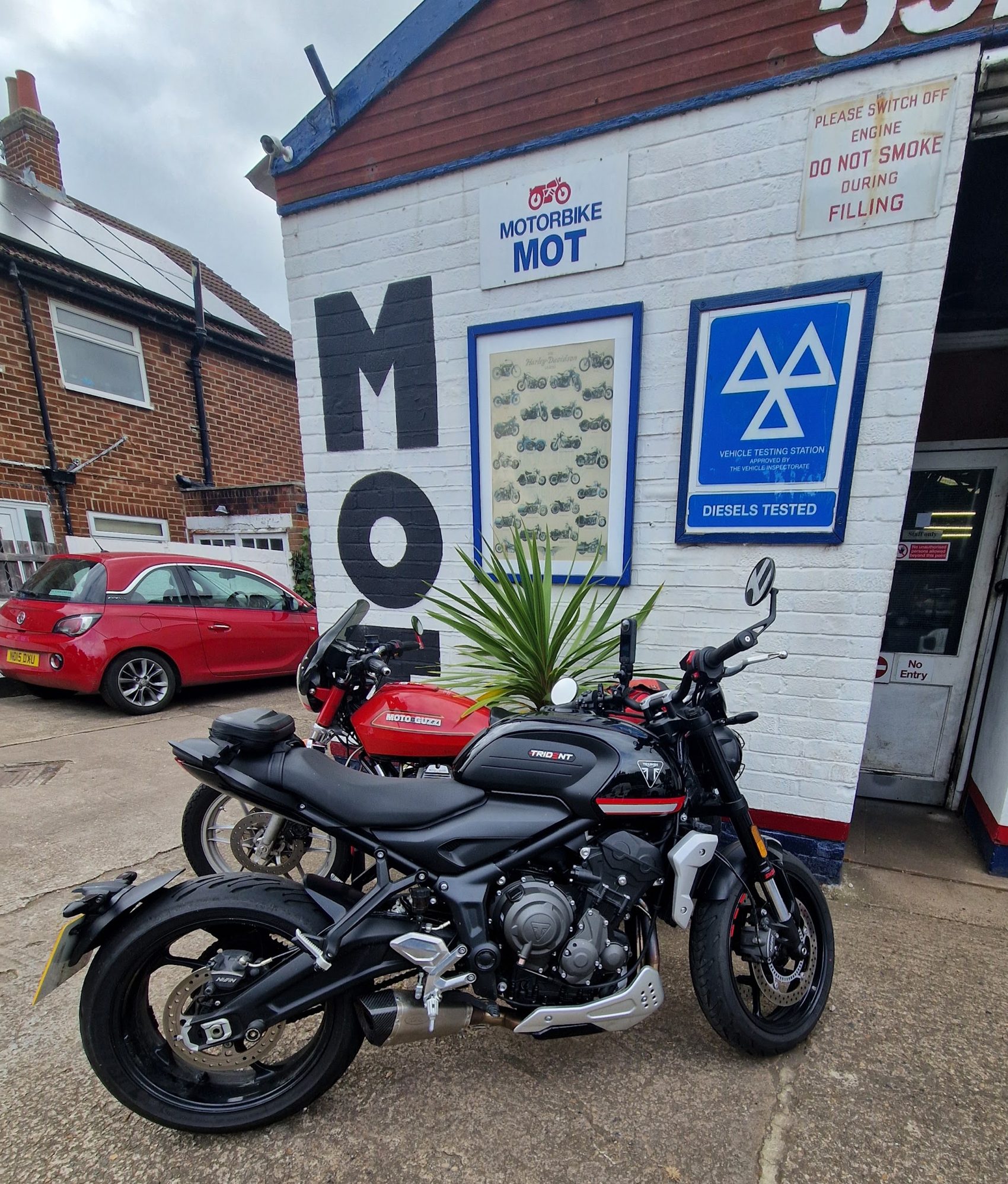 The painted MOT wall with the blue MOT sign and two motorbikes parked in front