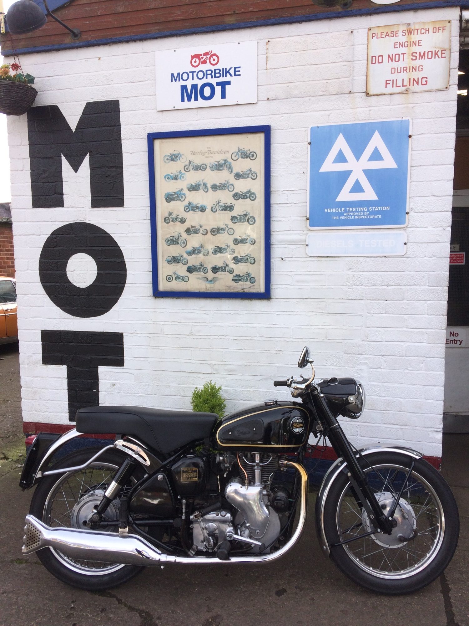 A black vintage motorbike parked in front of the white MOT wall